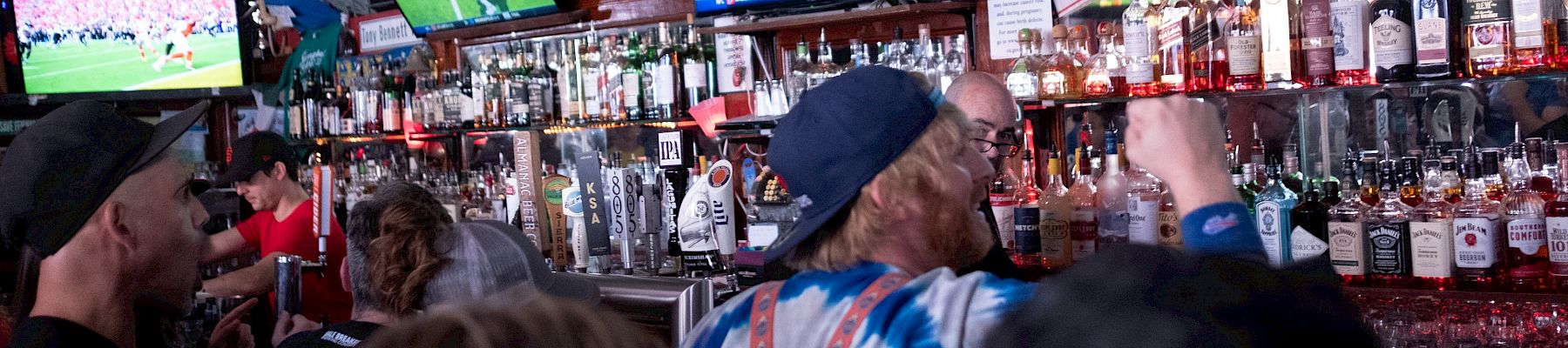A crowded bar with people watching sports on TV screens.