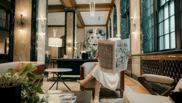 A person reads a newspaper in an elegant lounge with marble walls and modern decor.