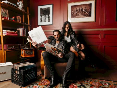 A man and woman in a cozy room with records, vintage decor, and framed photos, looking at vinyl albums.