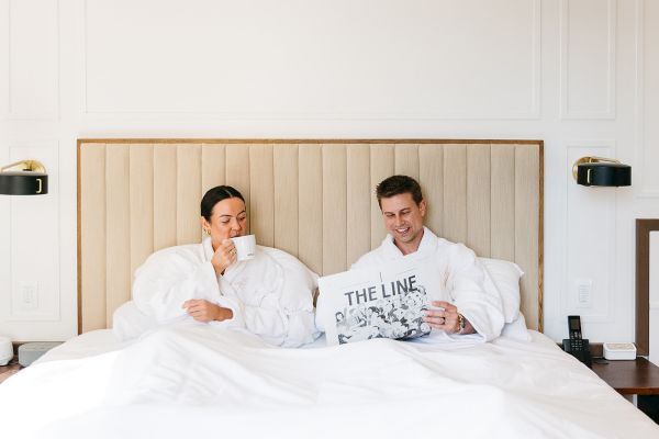Two people in bed, one drinking coffee, the other reading a newspaper.