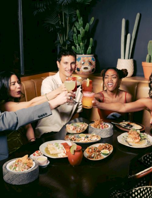 People raising glasses around a table with food and cacti decor.