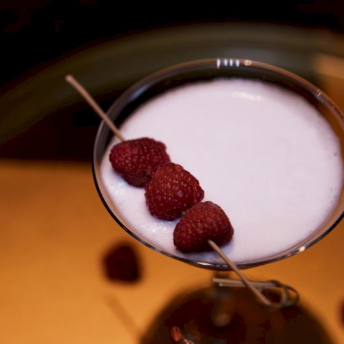 A cocktail with raspberries on a skewer.