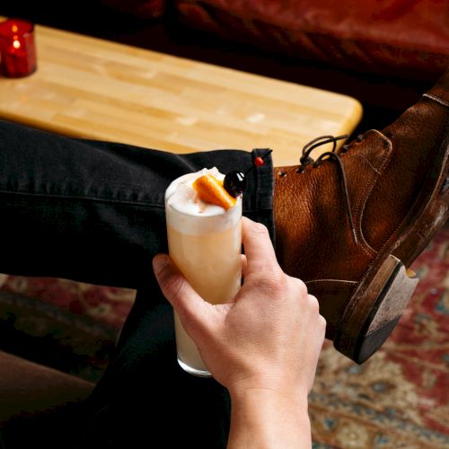 A person holding a cocktail with garnish, sitting relaxed.