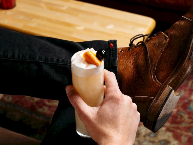 A person holding a cocktail with garnish, sitting relaxed.
