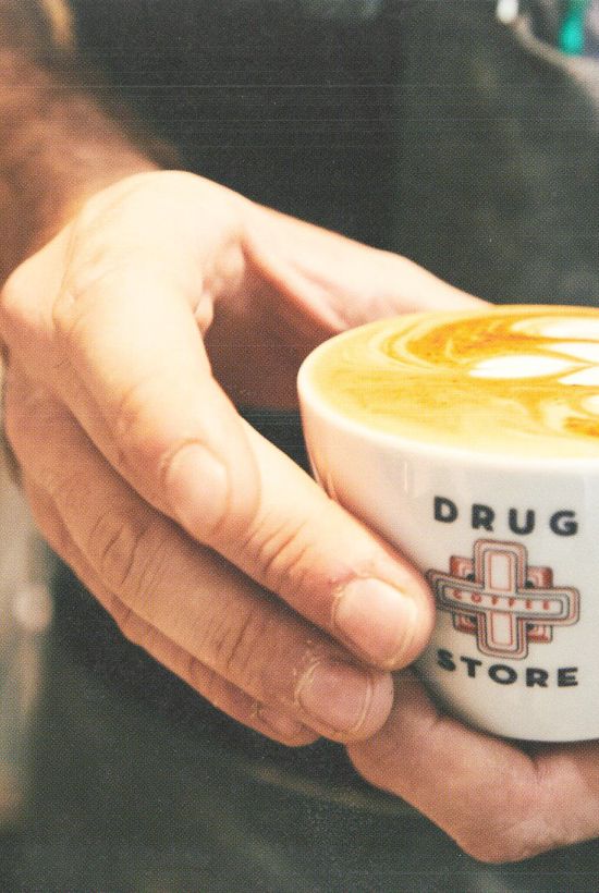 A person holding a cup of cappuccino with latte art.