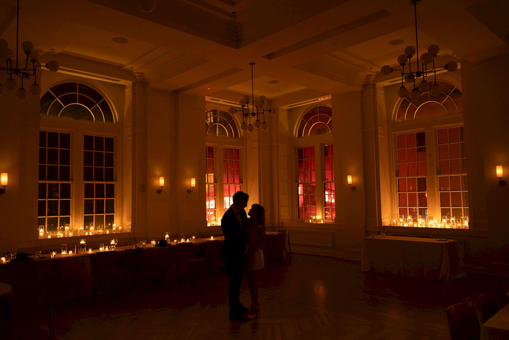 A couple stands in a dimly lit room with candles and large windows.