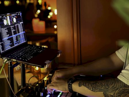 A DJ is mixing tracks on a turntable with a laptop in a dimly lit setting, creating a vibrant ambiance with atmospheric lighting.