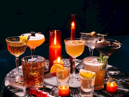 A variety of cocktails and candles on a dark table, creating a cozy, atmospheric vibe.