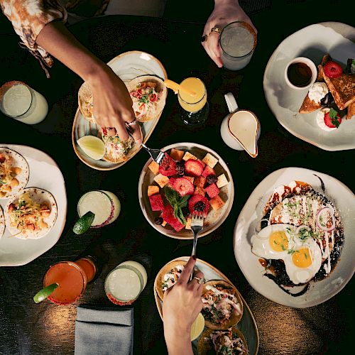 A variety of dishes including tacos, fruit, and drinks on a table.