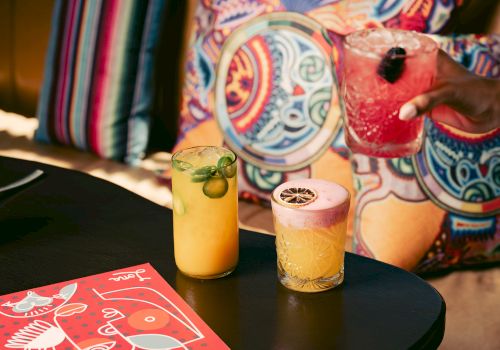 Colorful cocktails on a table with vibrant pillows in the background.