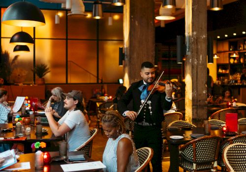 A lively restaurant with diners at tables and a musician playing the violin, all set in a warm, inviting atmosphere.