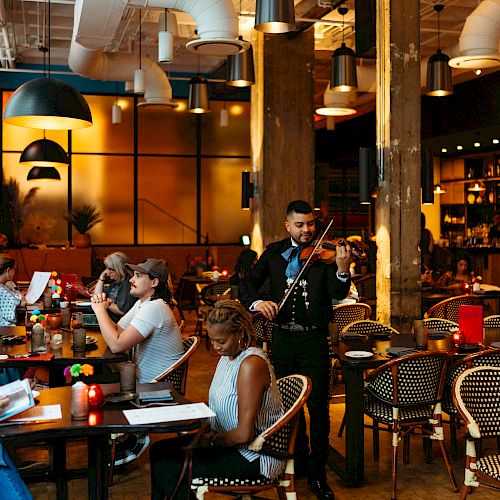 A lively restaurant with diners at tables and a musician playing the violin, all set in a warm, inviting atmosphere.