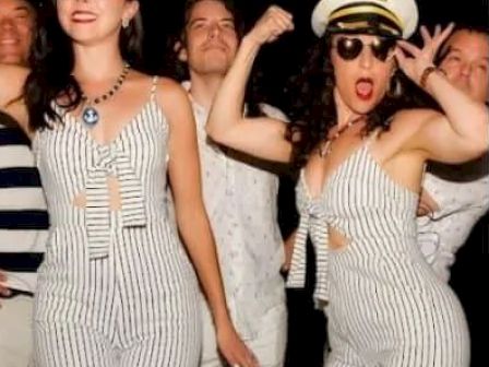 People in nautical-themed outfits and hats pose in a lively atmosphere, displaying a playful and stylish vibe.