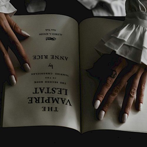 A person with elegant, ruffled sleeves holds open a book titled 