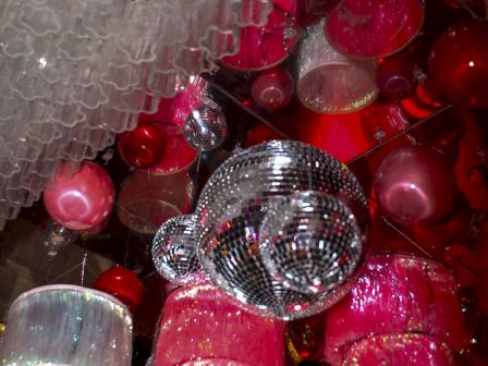 The image shows a collection of colorful, hanging light fixtures, including pink and red lampshades and a shiny silver disco ball.