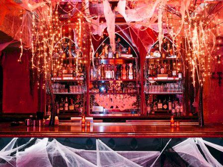 A decorated bar with cobwebs, lights, and bottles on shelves, creating a spooky Halloween atmosphere.