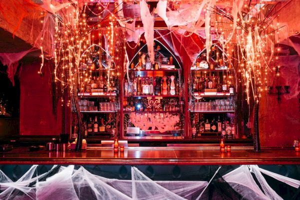 A decorated bar with cobwebs, lights, and bottles on shelves, creating a spooky Halloween atmosphere.