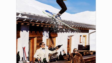A skier in formal wear holding drinks jumps over a snow-covered roof, while two people at an outdoor bar watch in amazement.