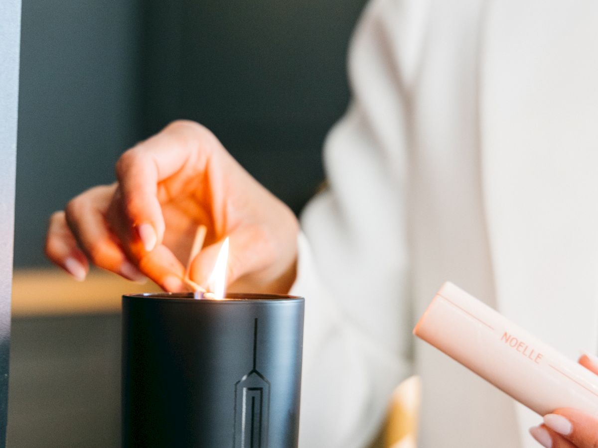 A person in white attire lights a black candle on a wooden surface using a lighter.