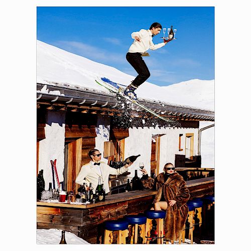 A skier jumps off a snowy roof holding a drink tray, while two people below enjoy drinks at an outdoor bar in a winter setting.