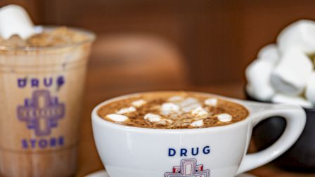 A cup of coffee with marshmallows and a cold drink on a wooden table.