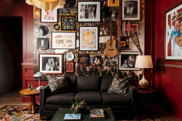 A cozy, eclectic living room with a black couch, musical instruments, photos, and art on a red wall; vibrant and artistic ambiance.