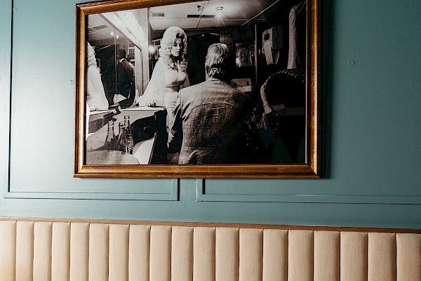 A bedroom with a cushioned headboard, striped pillow, and framed black-and-white photo on a teal wall, creating a cozy atmosphere.
