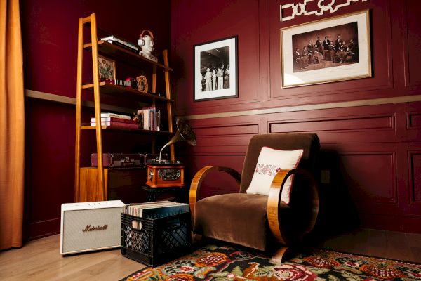 A cozy room with a retro chair, bookshelf, vintage radio, framed photos, and a Marshall amplifier on a colorful rug.