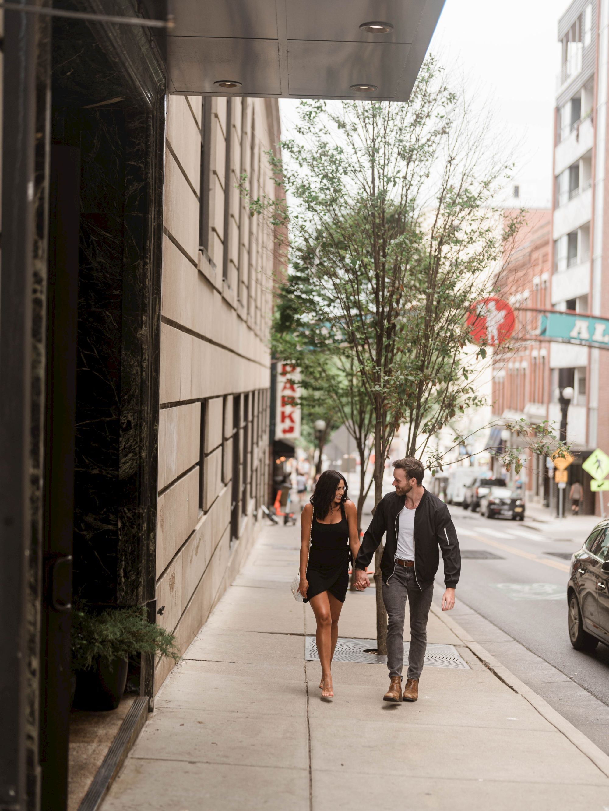 A couple holding hands, walking down a city sidewalk.