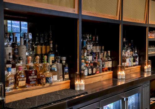 A bar shelf with various liquor bottles and lit candles.