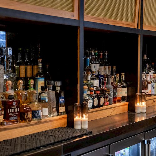 A bar shelf with various liquor bottles and lit candles.