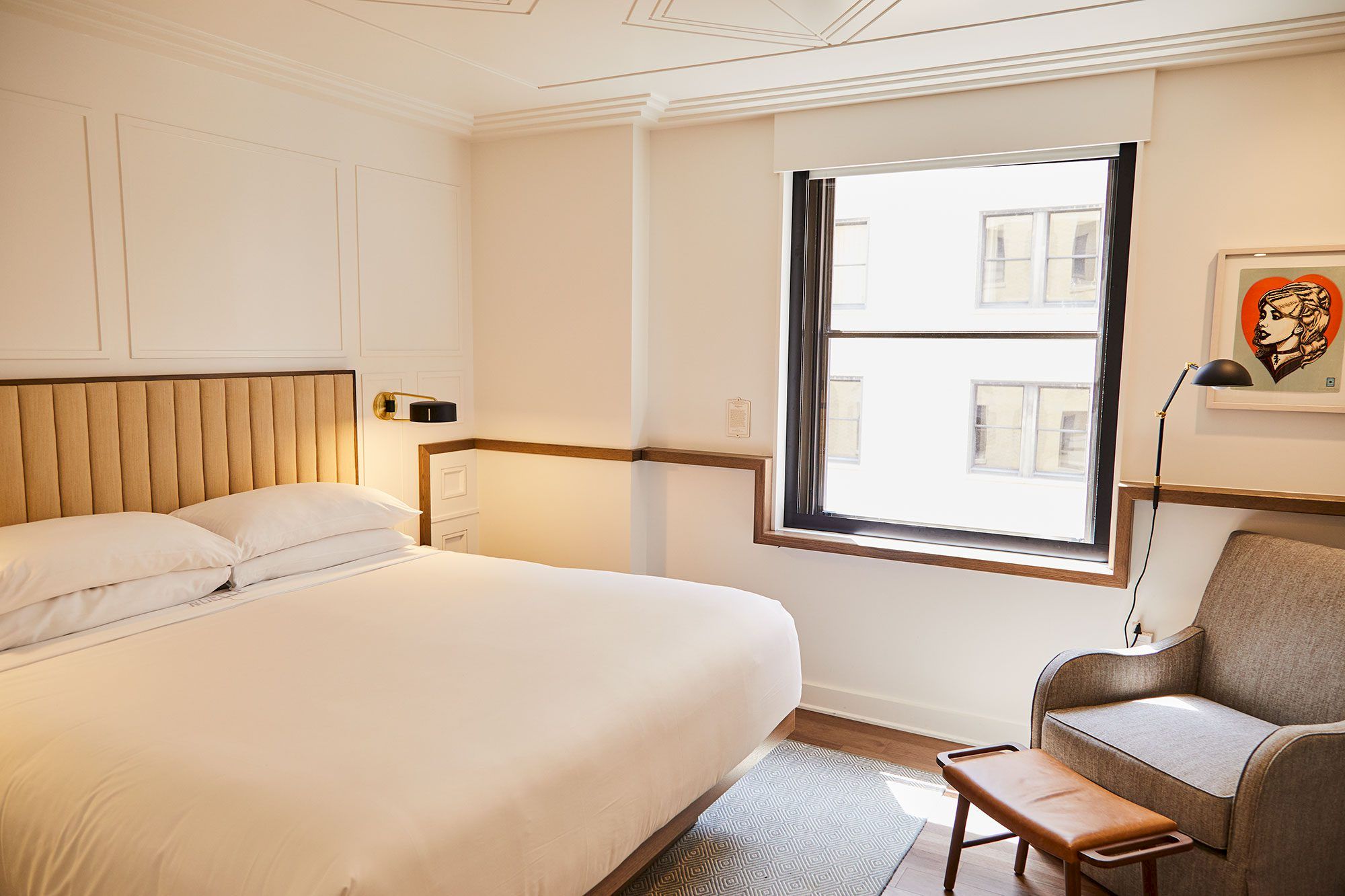 A modern hotel room with a bed, armchair, lamp, and window.