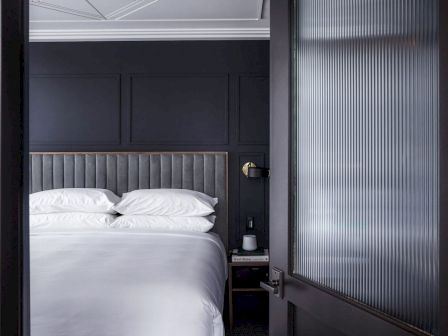A modern bedroom with a plush bed, navy walls, and a glass door.