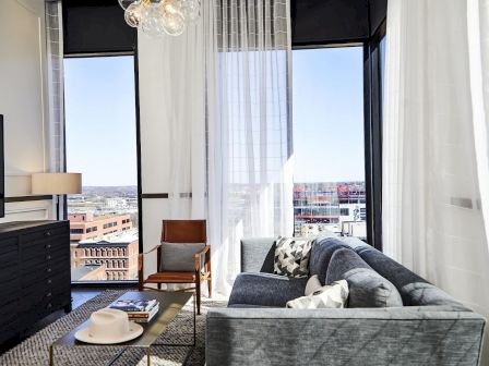 A modern living room with a couch, chair, lamp, and large windows with city views.