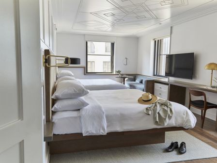 A modern hotel room with two beds, a desk, TV, and decorations.