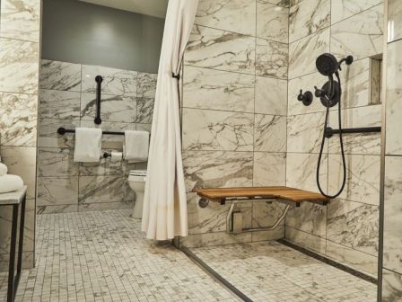 A modern bathroom with a marble shower, bench, and safety rails.