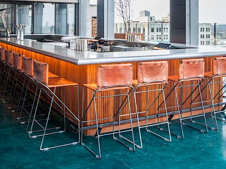 A modern bar with high metal chairs and a wooden counter.