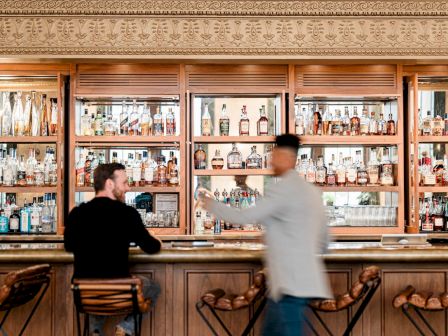 A bar with shelves of liquor, patrons, and ornate decor.
