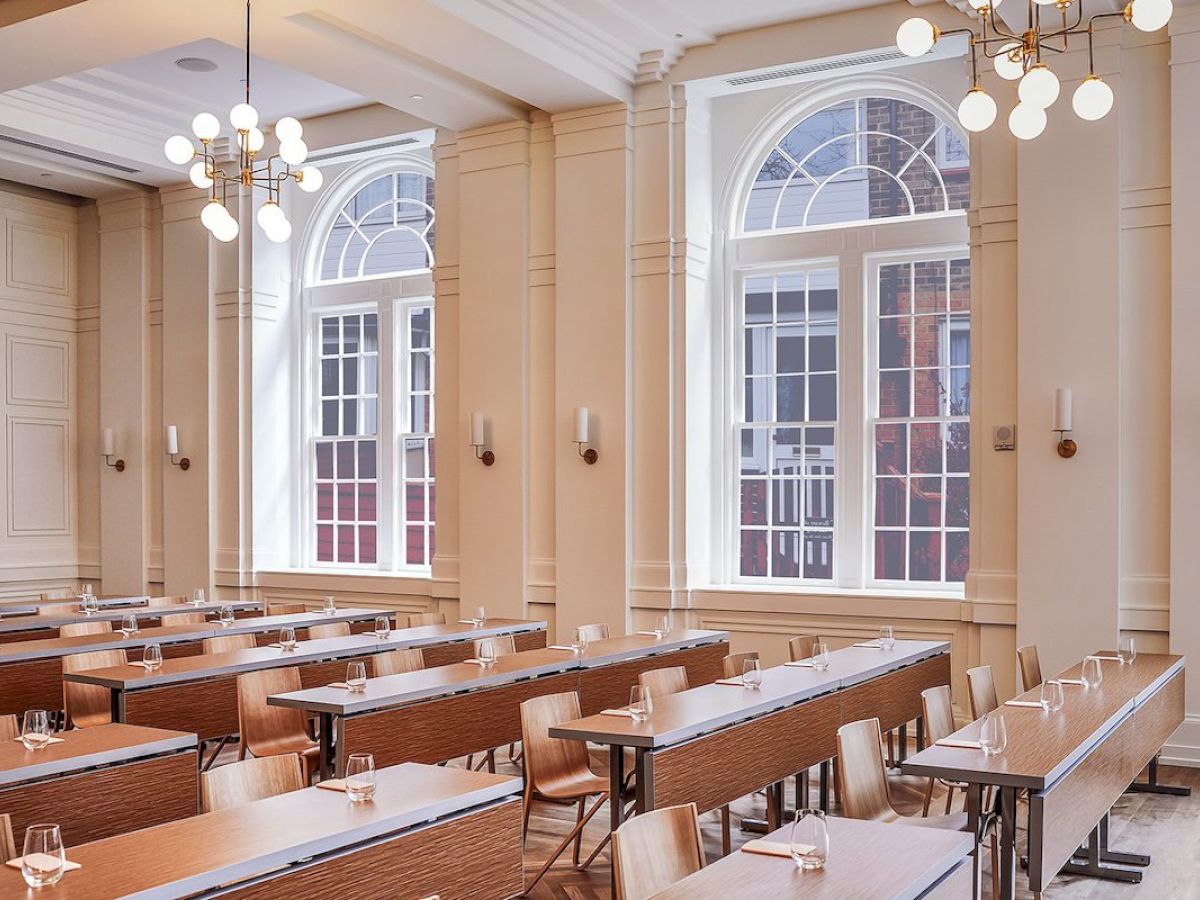 A bright room with rows of tables and chairs, featuring large arched windows.