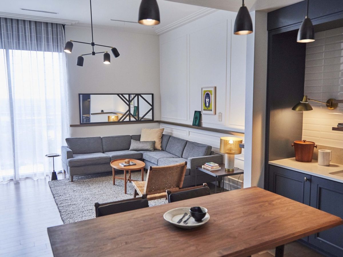 A modern living room and kitchen with a gray sofa and wooden table.