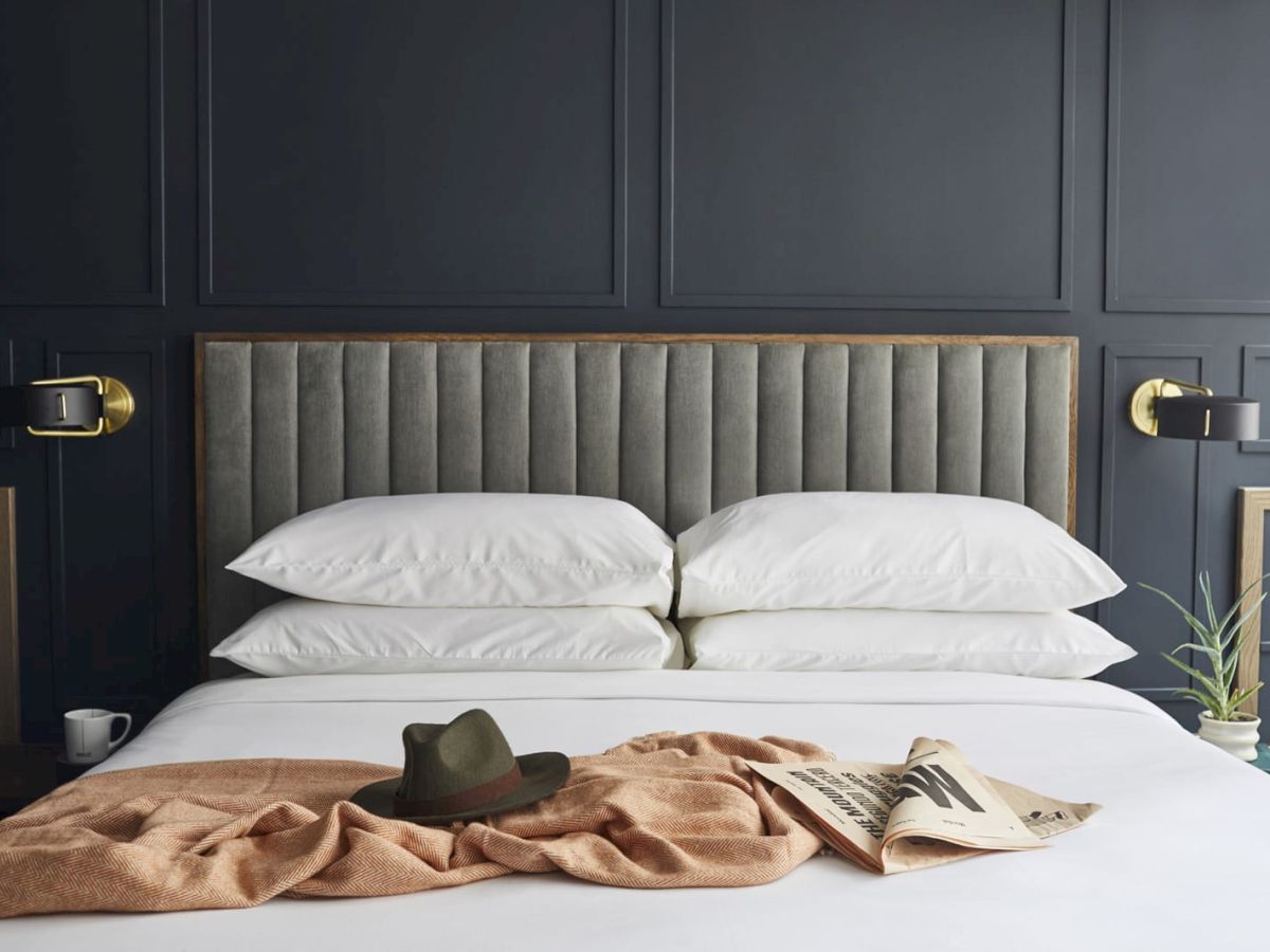 A bed with white pillows, a hat, a newspaper, and a blanket.