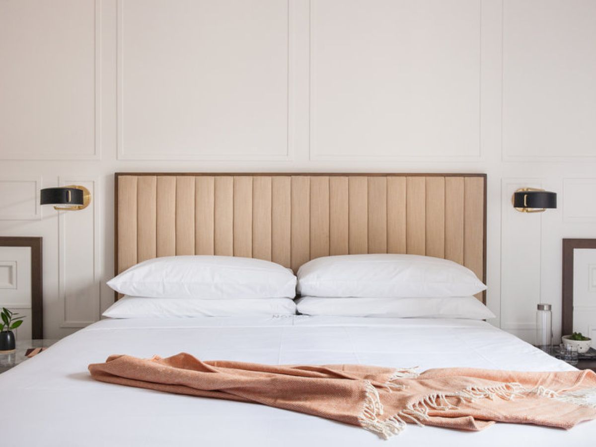 A neatly made bed with white pillows and a light brown throw blanket.