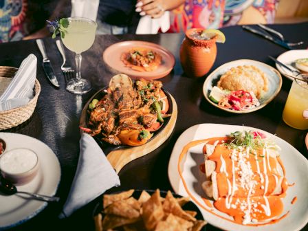 Variety of Mexican dishes with drinks on a table.