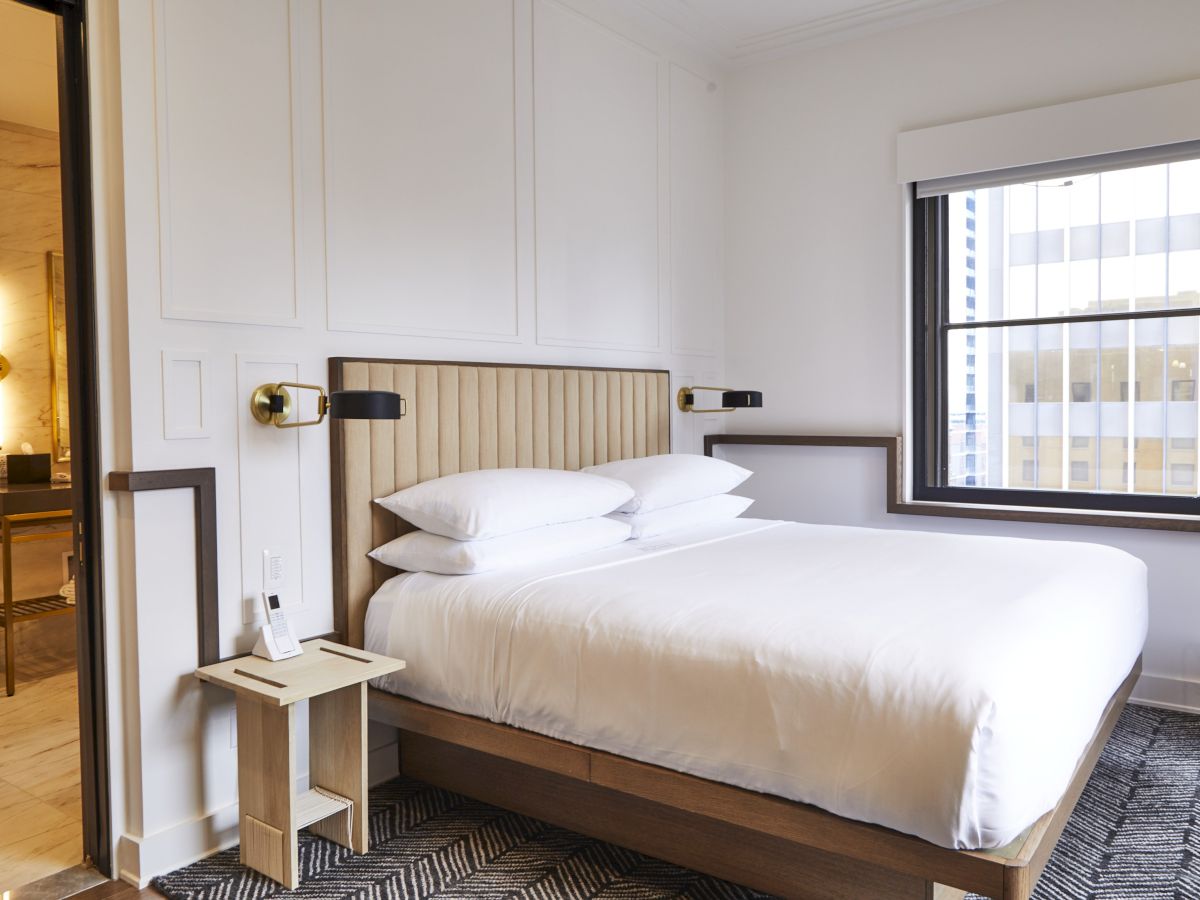 A modern hotel room with a bed, nightstand, and view of a building.