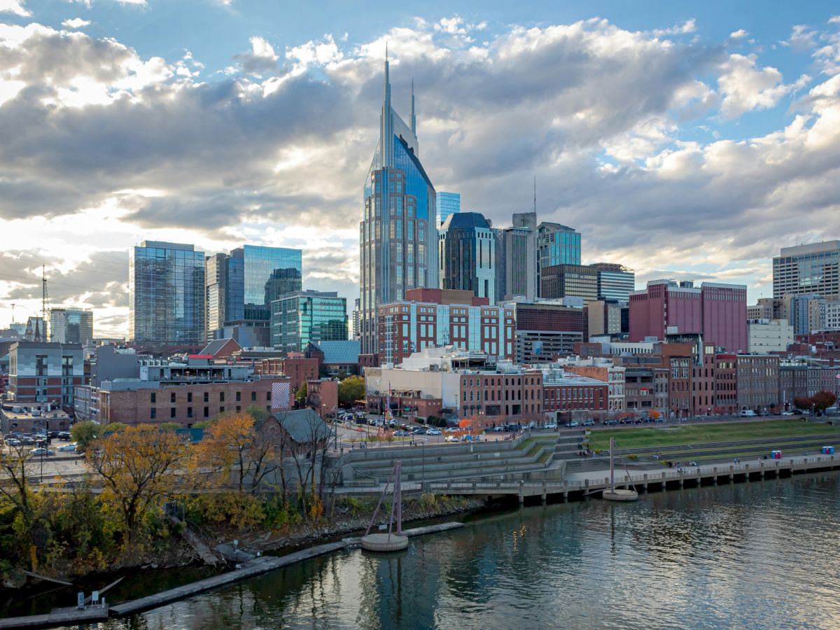 A city skyline with modern and historic buildings by a river under a cloudy sky.