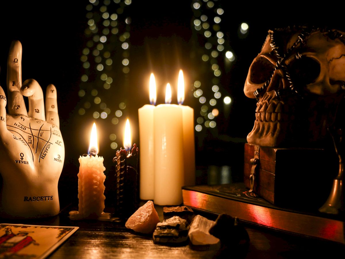 A mystical setup with candles, a skull, crystals, tarot card, and a palmistry hand model.