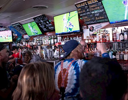 A crowded bar with people watching sports on TV screens.