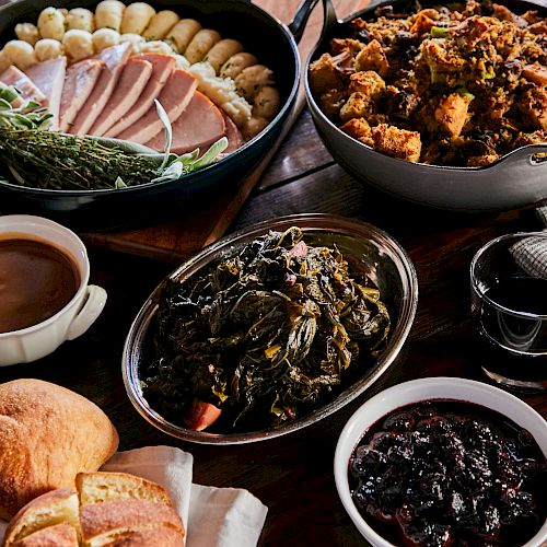 A meal with sliced ham, Brussels sprouts, stuffing, greens, bread, gravy, and a drink.