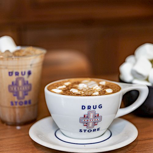 A cup of coffee and a drink with marshmallows on a wooden table.