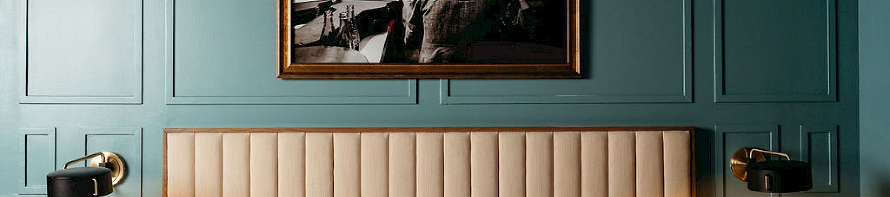 A bedroom with a framed photo above the bed and teal wall panels.